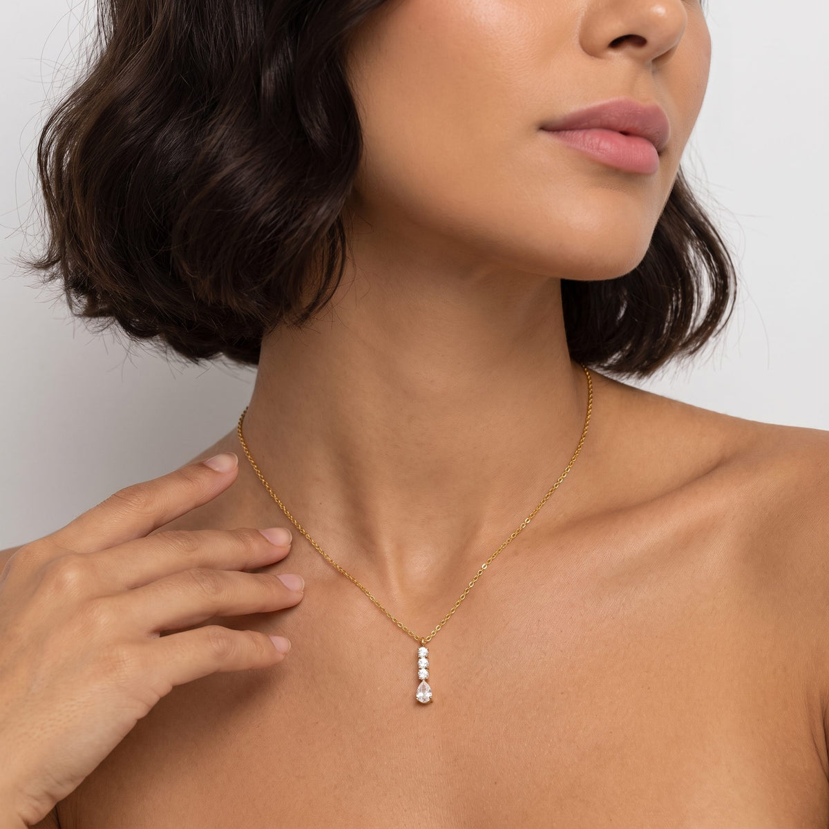 Woman with a dark bob wearing the Céleste pear drop gold necklace, one hand raised near her neck
