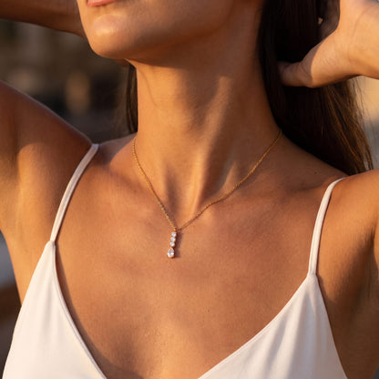 Woman in a white camisole wearing the Céleste pear drop gold necklace in warm evening light