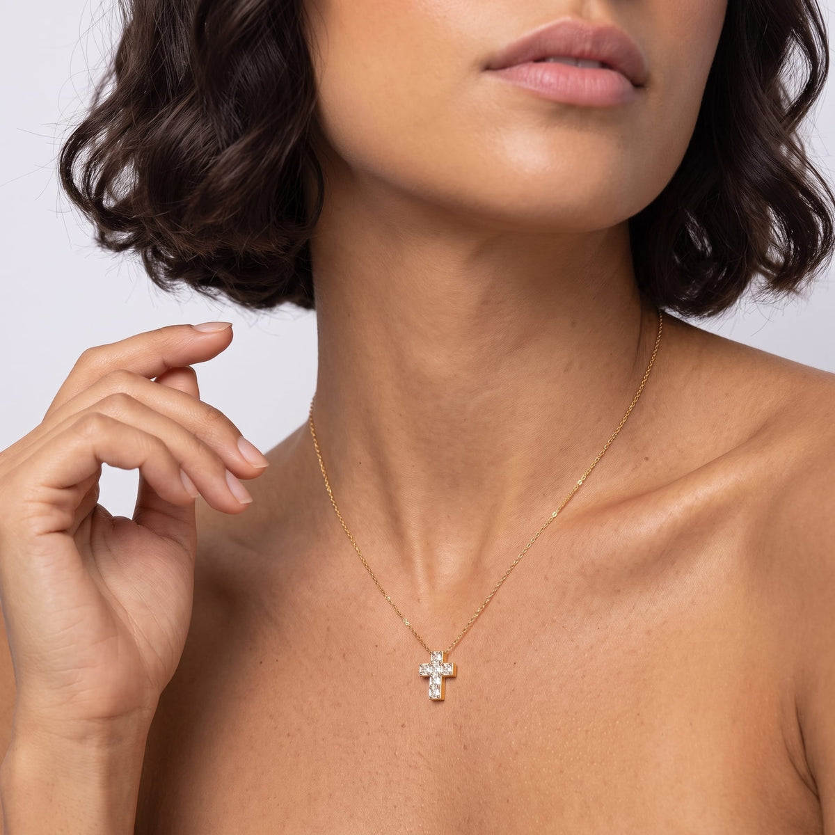 Woman wearing the Chiara crystal cross gold necklace at the collarbone with her hand raised