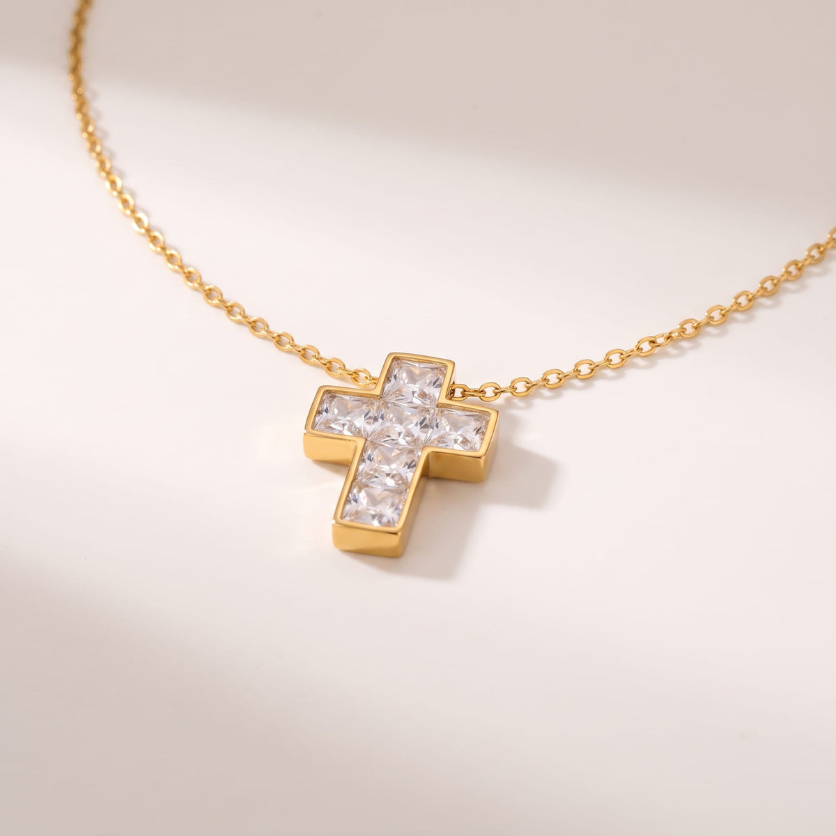 Chiara crystal cross gold necklace on a white surface with soft shadows