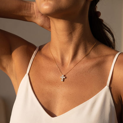 Woman wearing the Chiara crystal cross gold necklace at the collarbone in warm sunlight