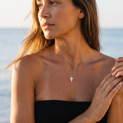 Woman wearing the Chiara crystal cross gold necklace at the collarbone near the ocean