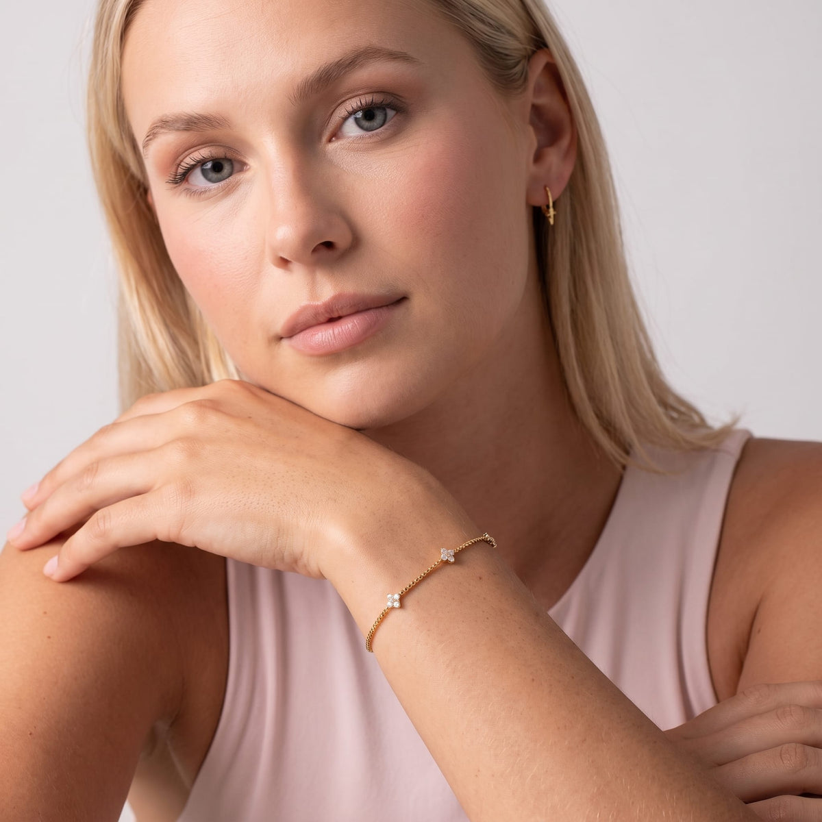 Woman wearing the Clara crystal clover gold bracelet on the wrist while resting her chin on her hand