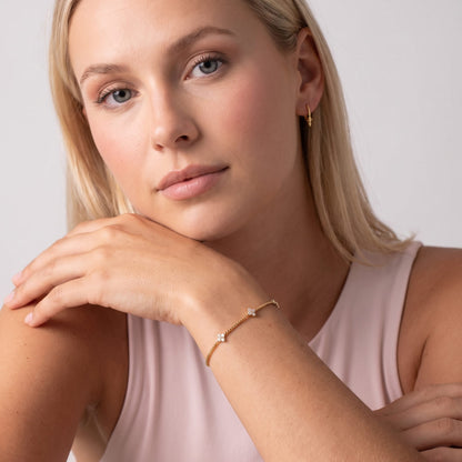 Woman wearing the Clara crystal clover gold bracelet on the wrist while resting her chin on her hand