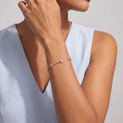 Woman wearing the Clara crystal clover gold bracelet on the wrist with a light blue top