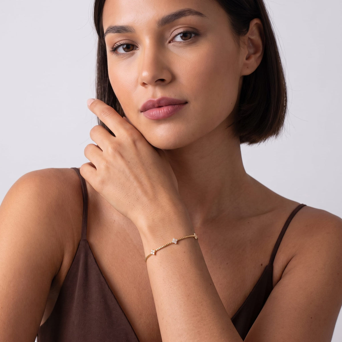Woman wearing the Clara crystal clover gold bracelet on the wrist in a brown strap dress