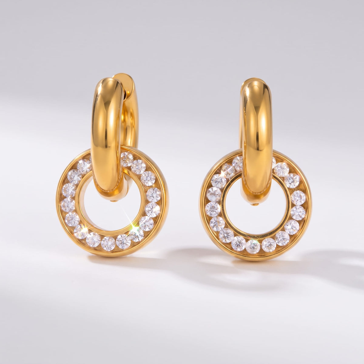 Clémence circle huggie gold earrings on a plain white surface showcasing channel-set zircon charms