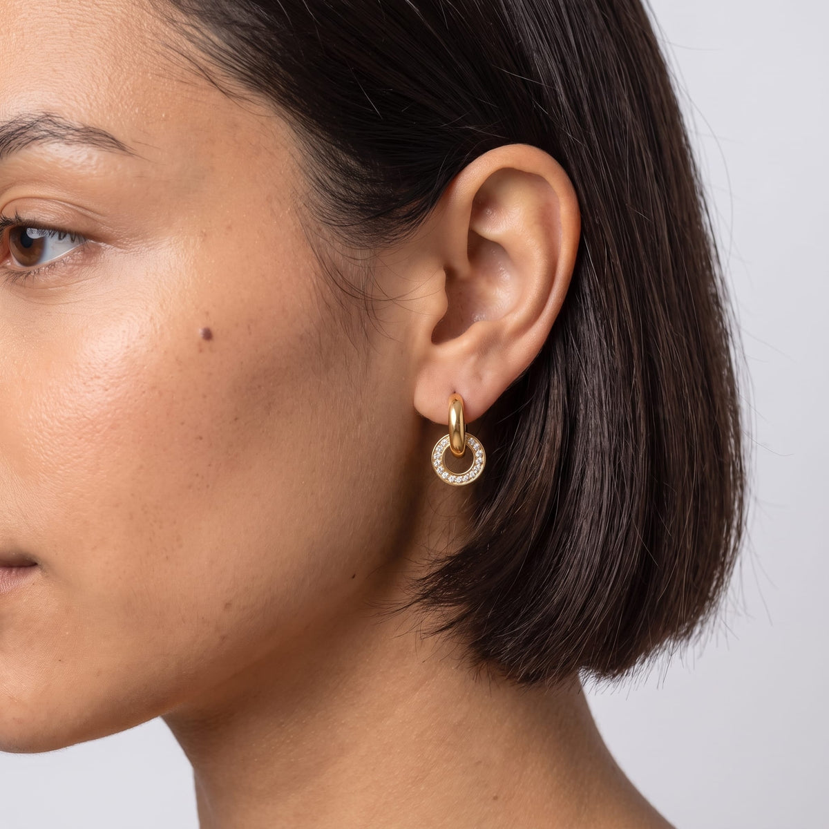Woman wearing the Clémence circle huggie gold earrings on the ear with short dark hair in profile