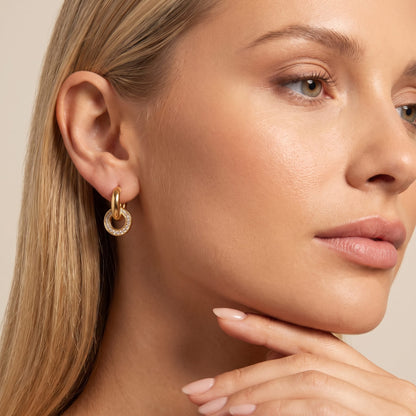 Woman wearing the Clémence circle huggie gold earrings on the ear touching her chin with her hand