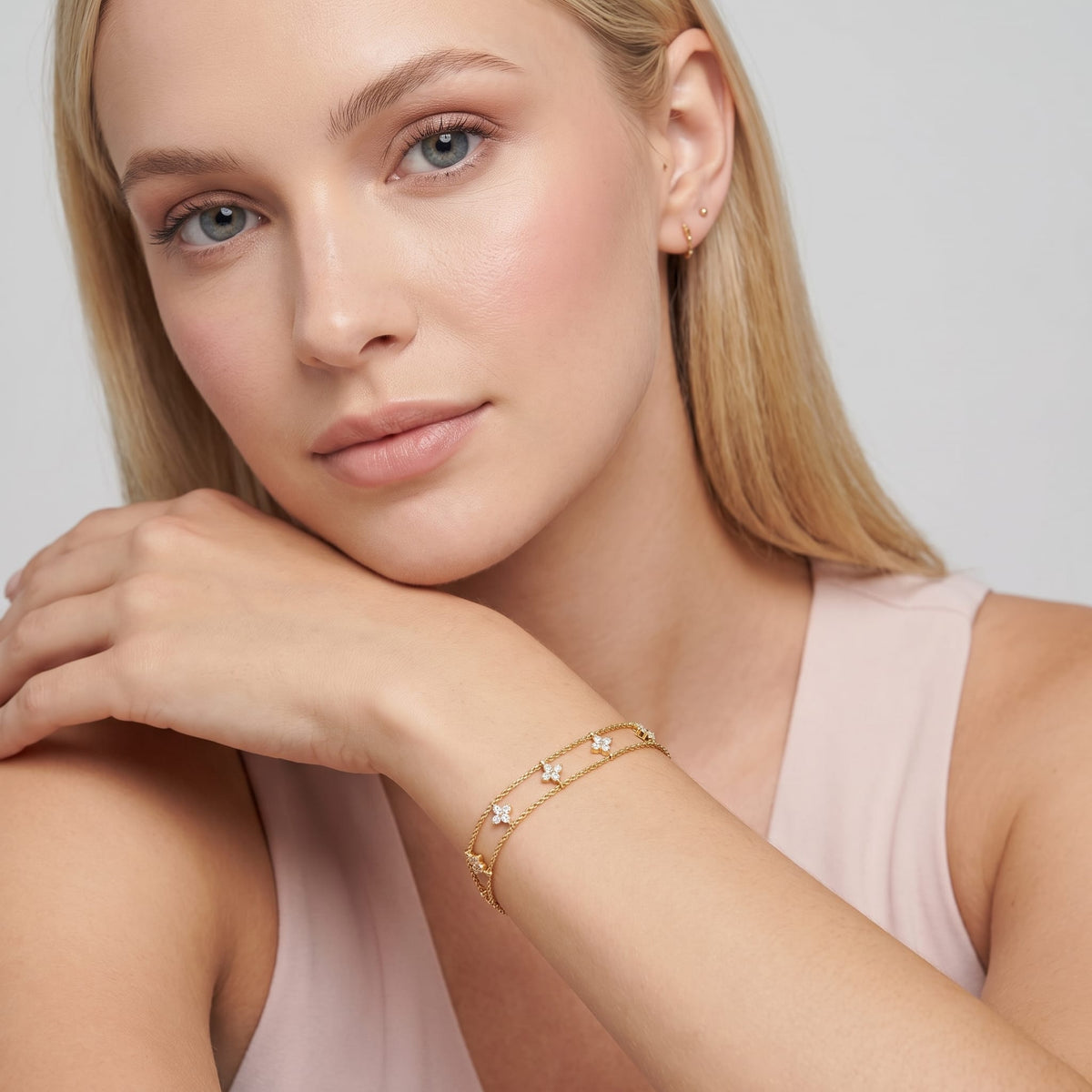 Woman wearing the Clémence layered clover gold bracelet on the wrist with her hand resting on her shoulder