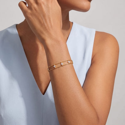 Woman wearing the Clémence layered clover gold bracelet on the wrist in a light blue top
