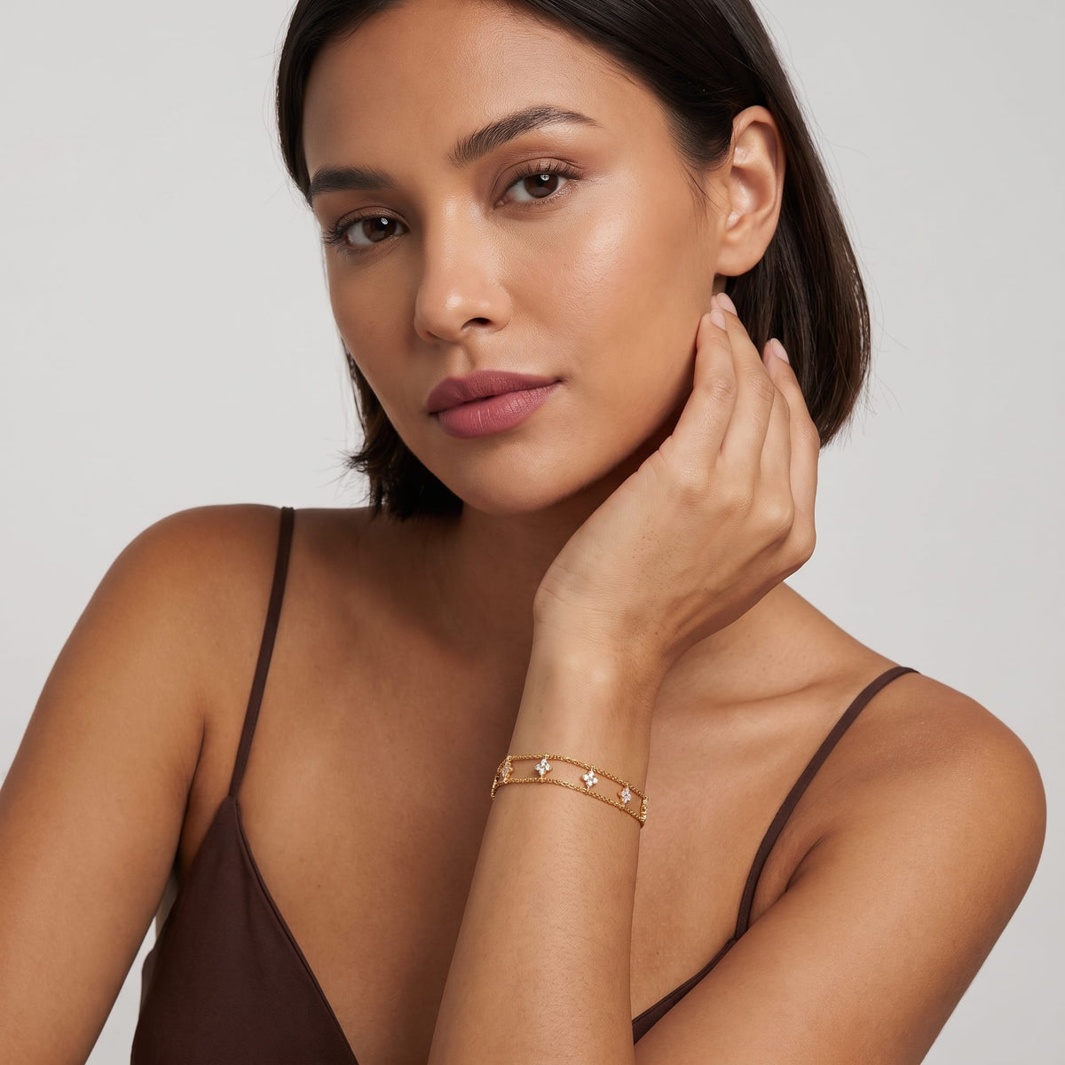 Woman wearing the Clémence layered clover gold bracelet on the wrist posing with hand near her chin
