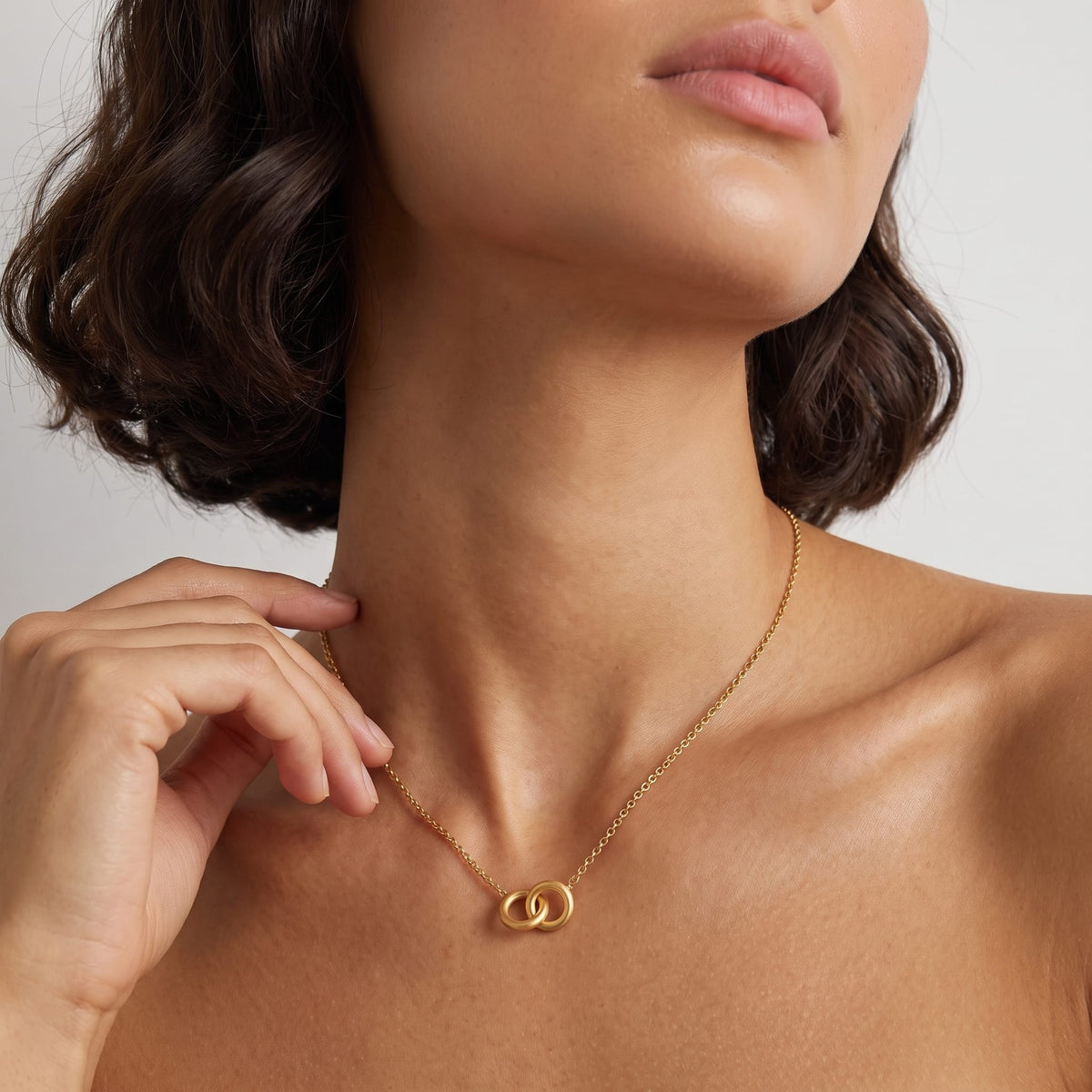 Woman wearing the Colette interlocking rings gold necklace at the collarbone with her hand raised near her neck