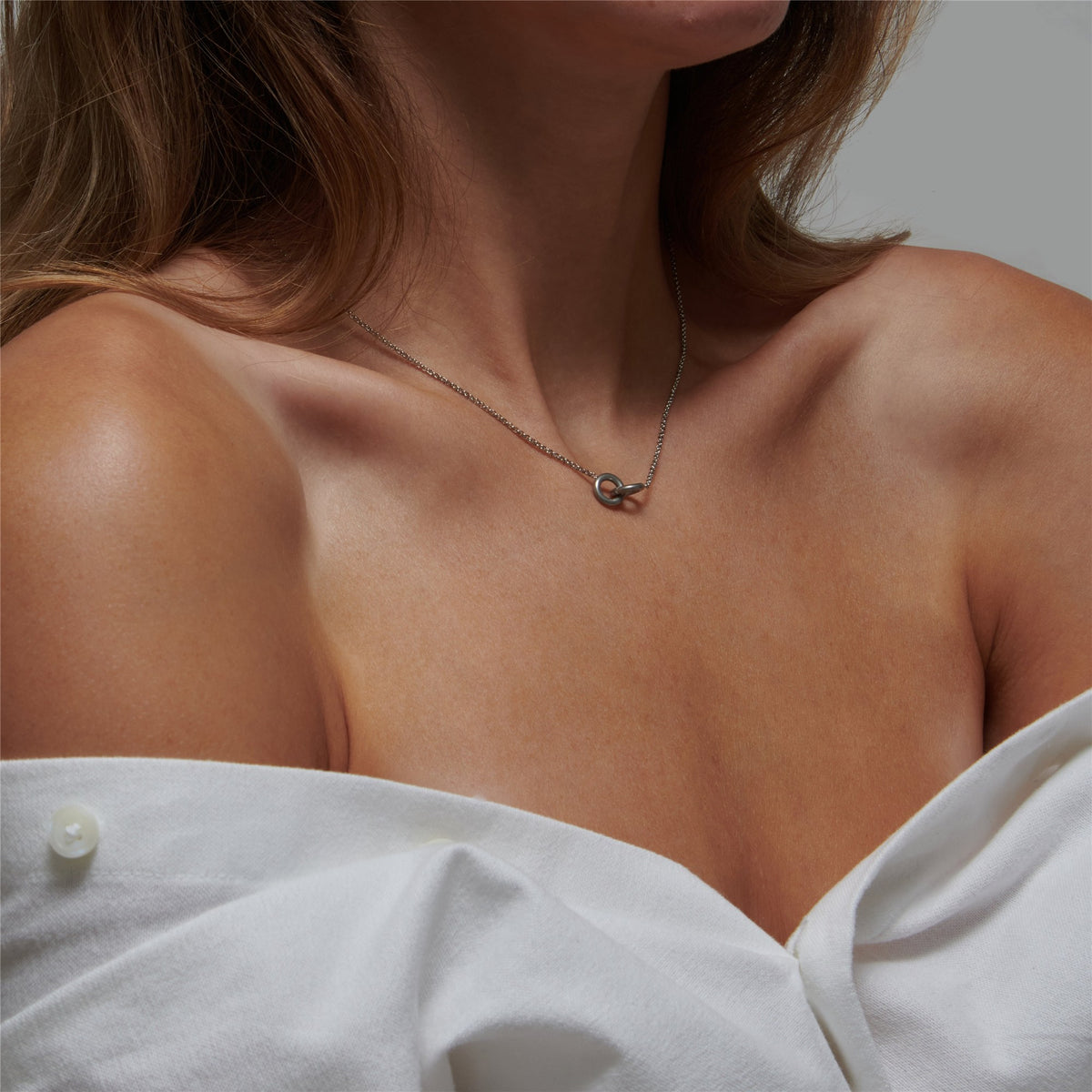 Woman in an off-shoulder white shirt wearing the Colette silver interlocking rings at the collarbone