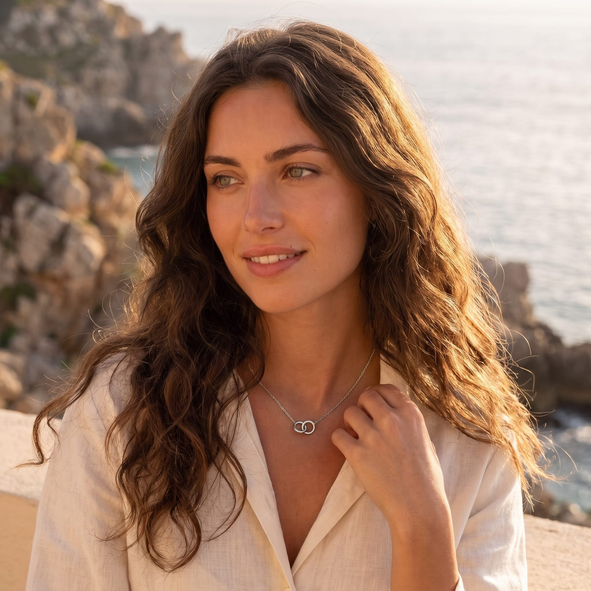Woman wearing the Colette interlocking rings silver necklace at the collarbone in a beige linen shirt outdoors