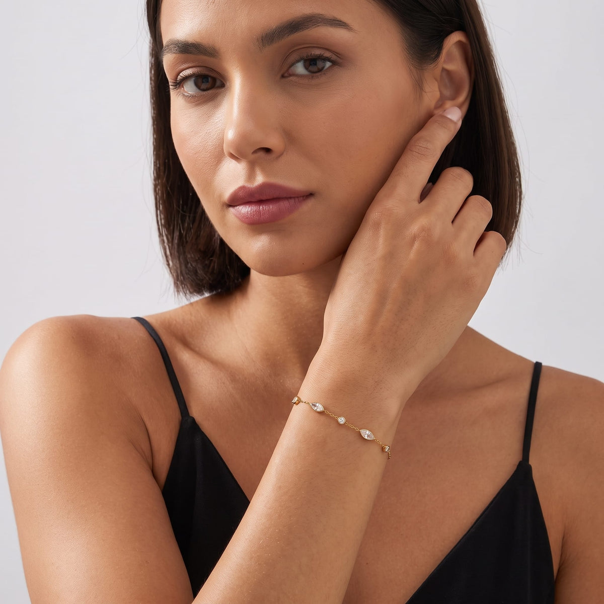 Woman wearing the Cosima marquise station gold bracelet on the wrist touching her chin