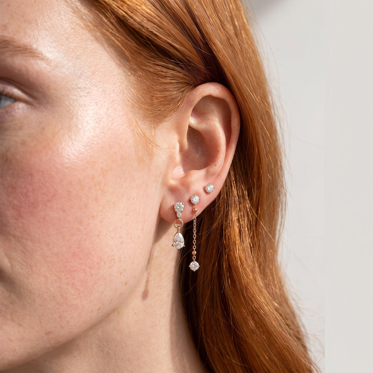 Wider view of a woman wearing the Delfina drop trio gold earrings on the ear, framed by red hair