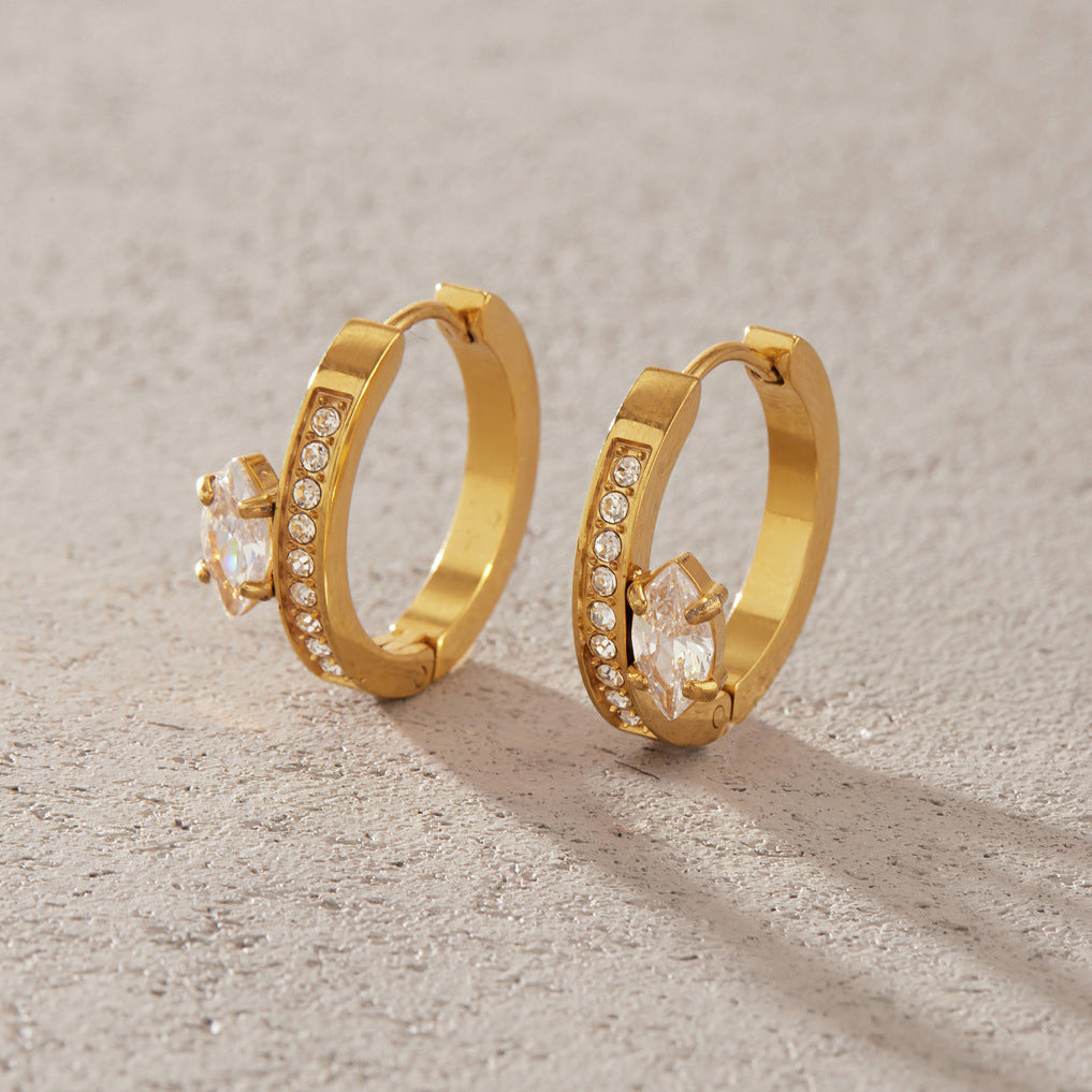 Pair of Diletta pavé huggie hoops with marquise crystals standing on a sandy stone surface