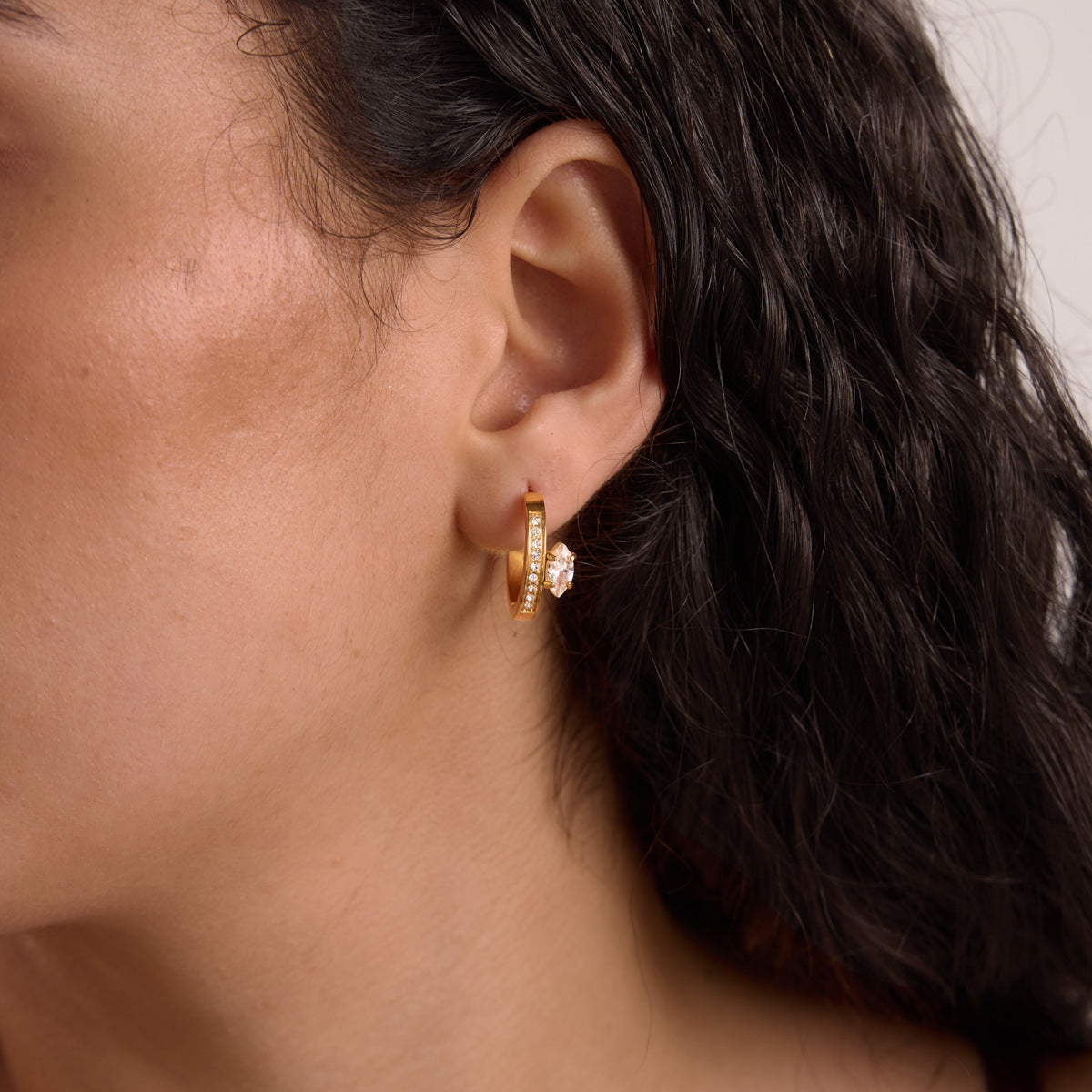 Woman with dark wavy hair wearing a Diletta crystal huggie hoop on her earlobe