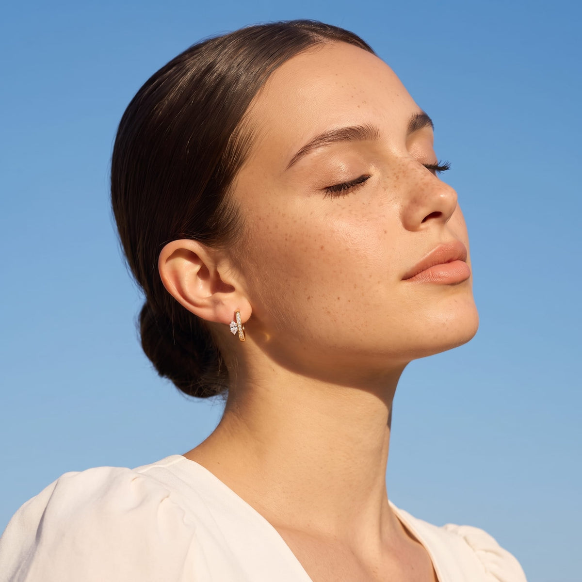 Woman wearing the Diletta marquise huggie gold earrings on the ear under blue sky