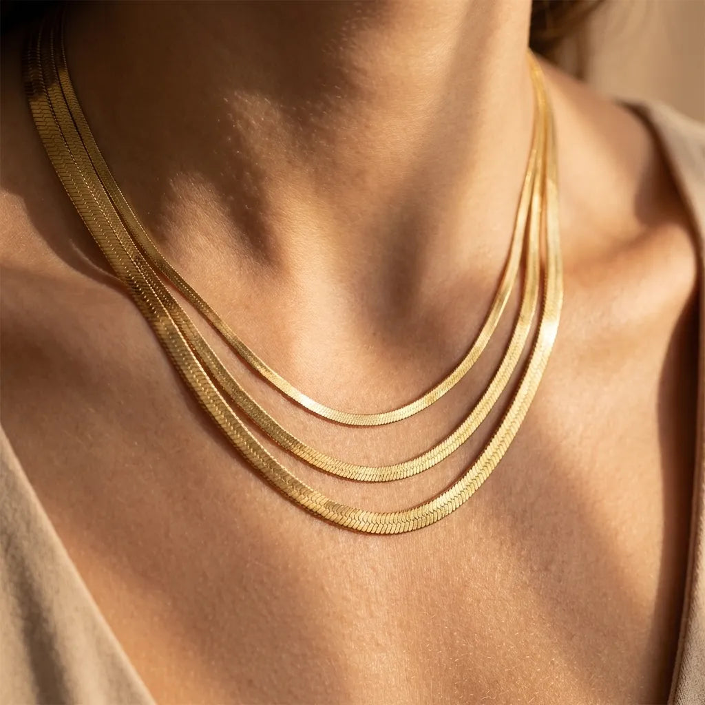 Woman wearing three Elizabeth gold herringbone necklaces in different widths, layered at the neckline