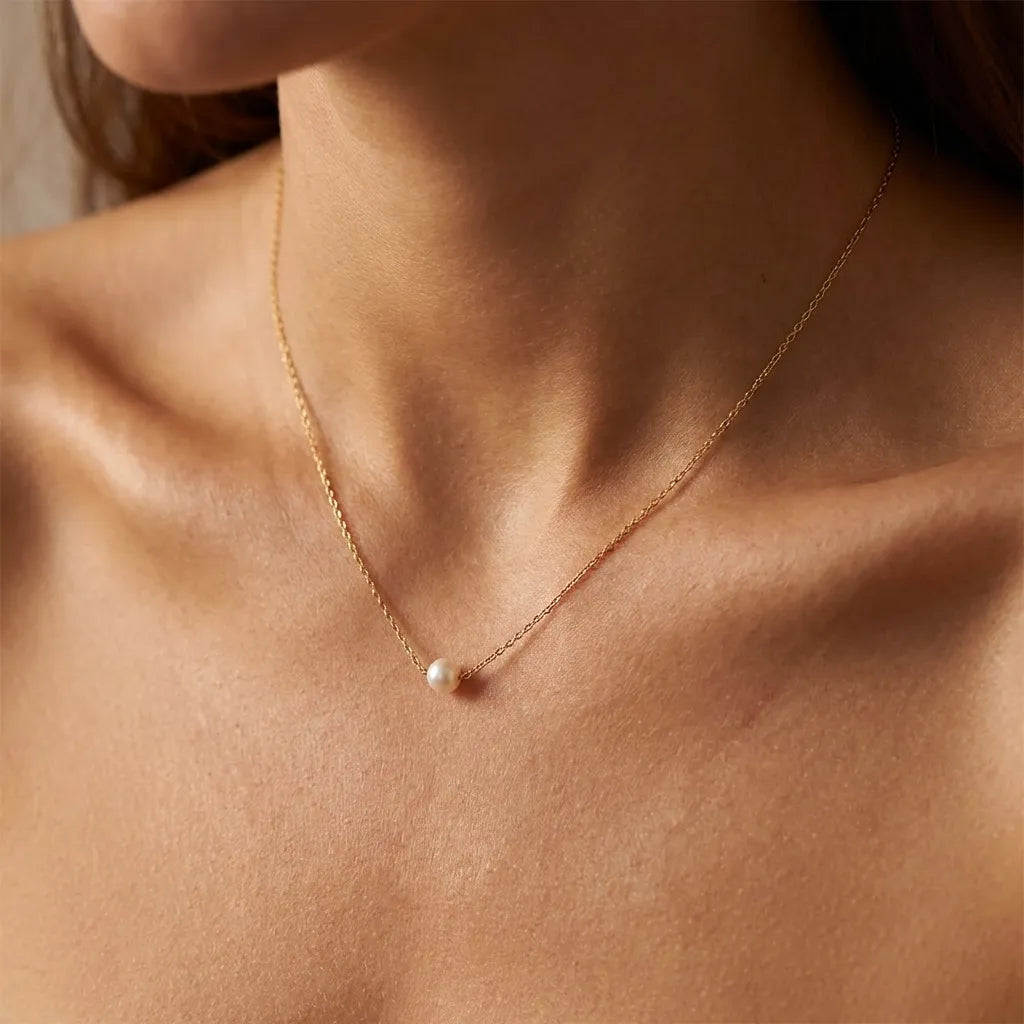 Woman wearing the Marianne gold necklace with a single small floating pearl at the collarbone