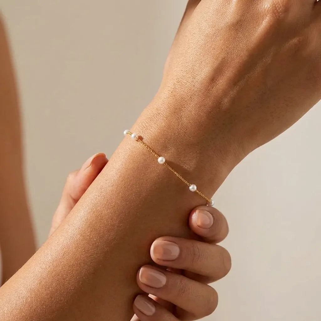 Woman wearing the Élise Dainty Pearl bracelet in gold, small pearls spaced along a fine chain