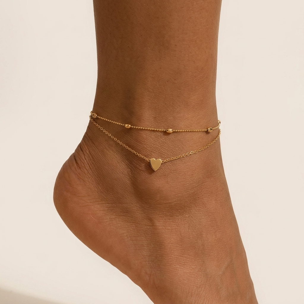 Silvia gold heart anklet on the ankle, beaded chain layered above a fine chain with a small heart
