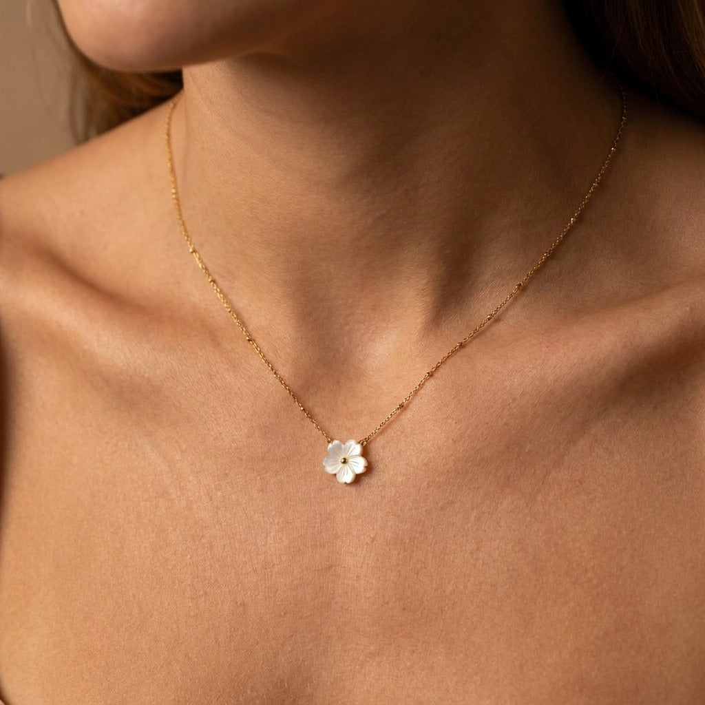 Woman wearing the Flora gold necklace with a white shell flower pendant on a beaded satellite chain