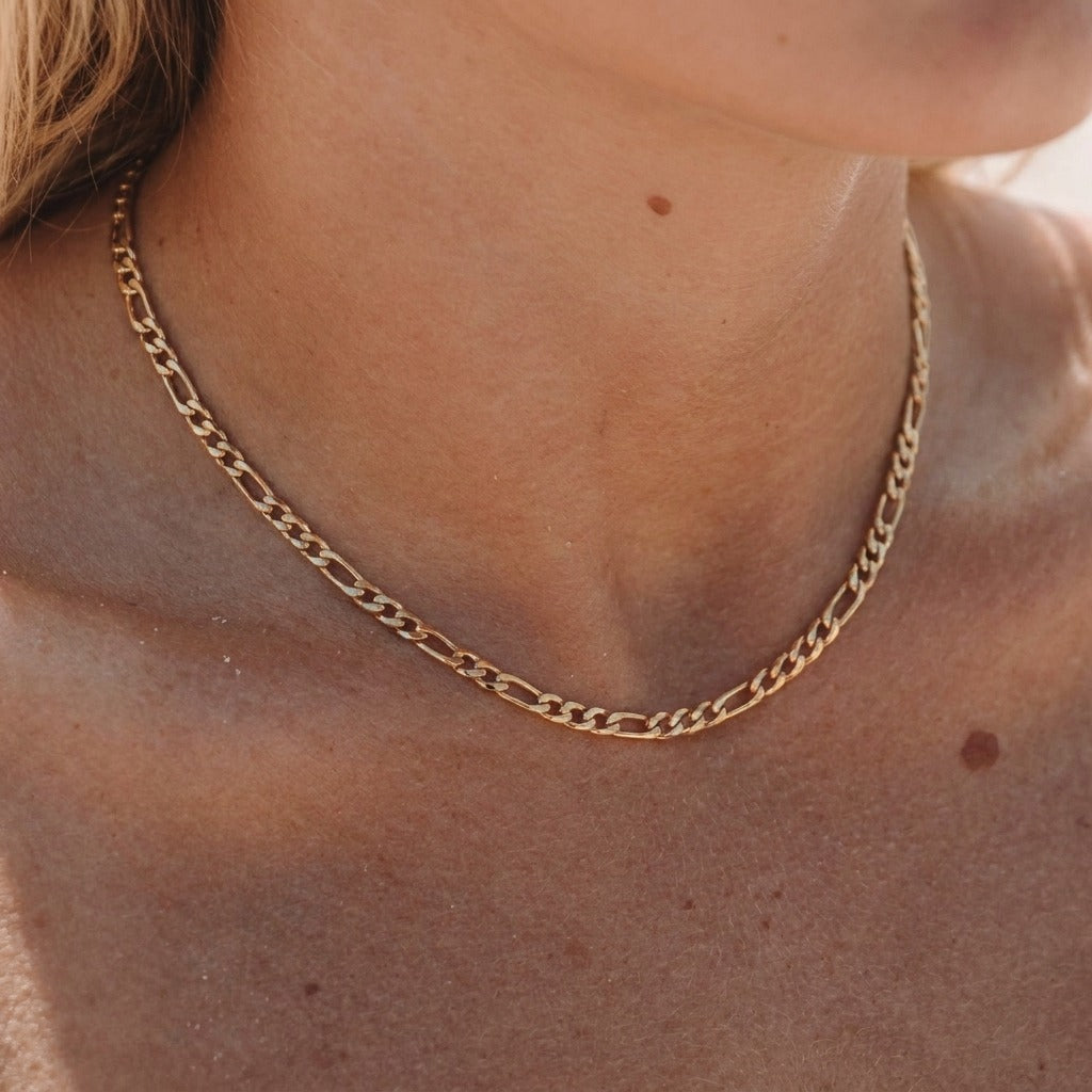 Woman wearing the Fiona gold Figaro chain necklace at the base of the neck in warm sunlight