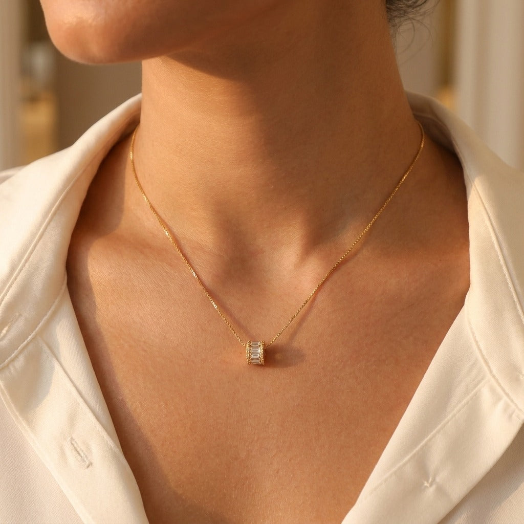 Woman in a white shirt wearing the Maia gold box chain necklace with a baguette crystal barrel pendant