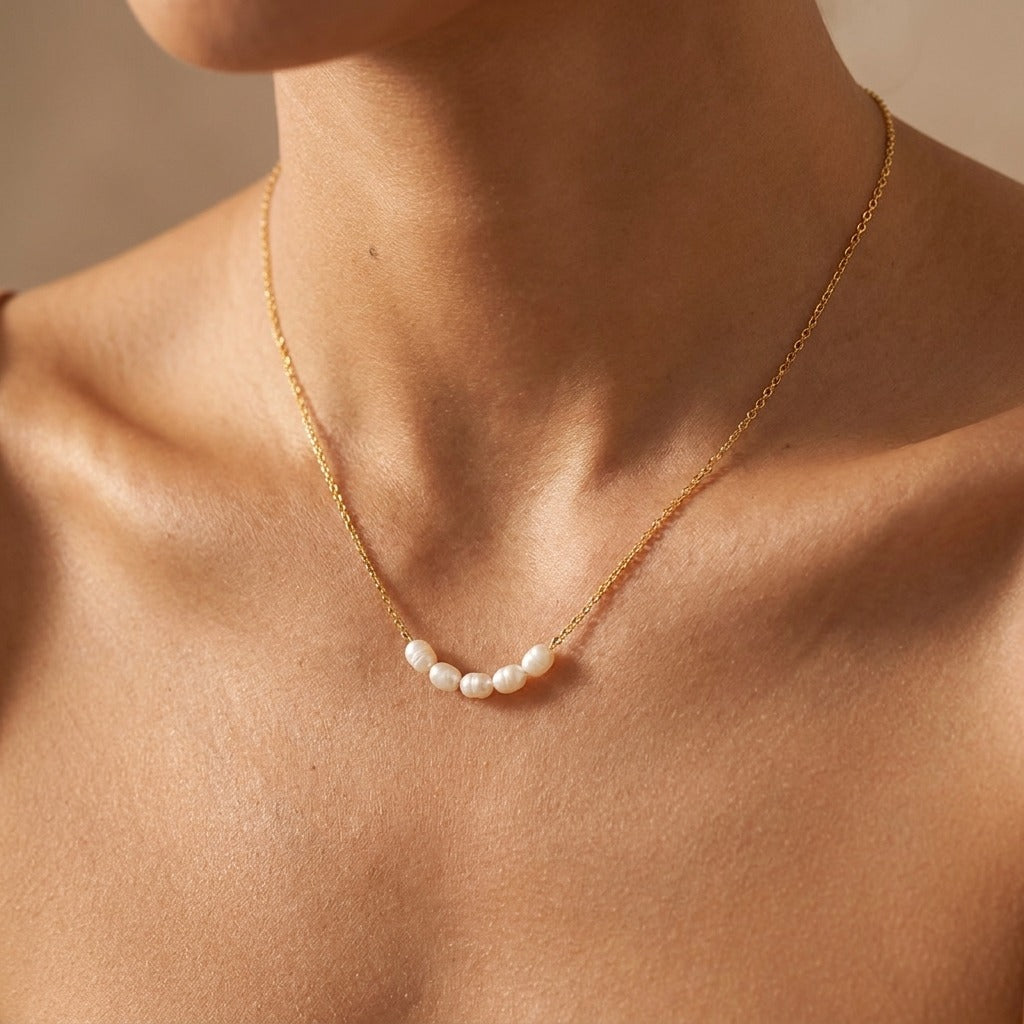 Woman wearing the Elle gold necklace with a short row of small pearls at the collarbone