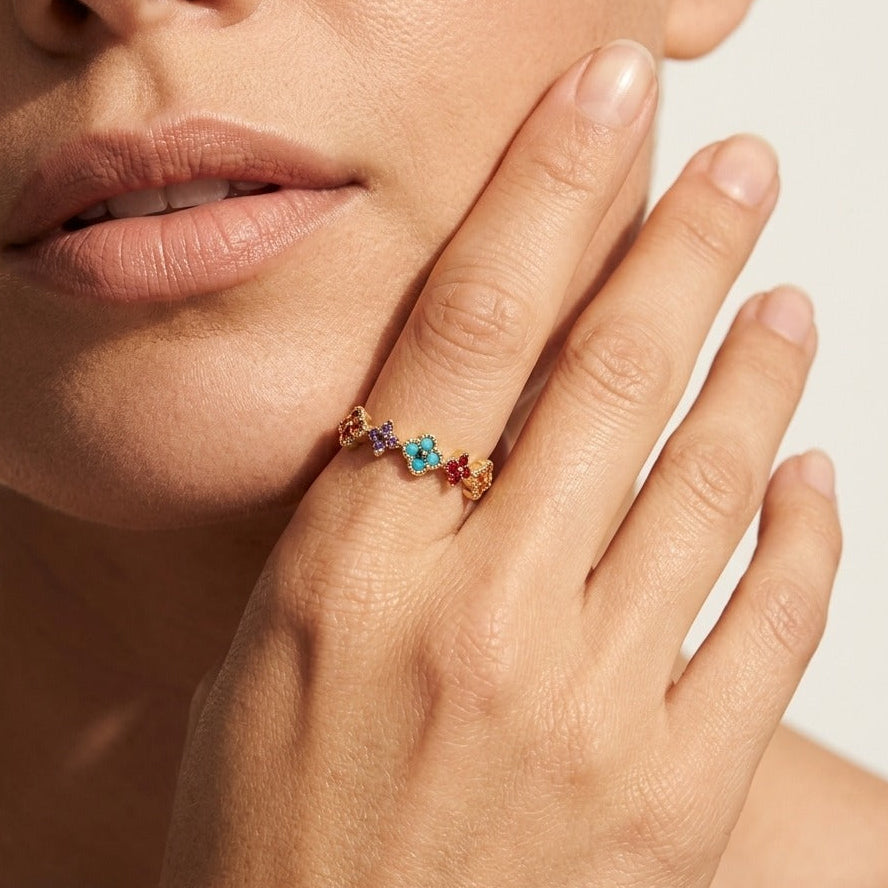Hand at the cheek wearing the Aurélie gold cluster ring with a row of multicolor flower clusters