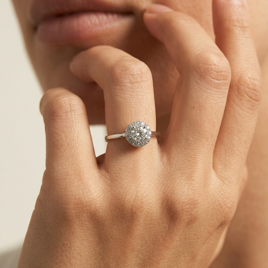 Woman wearing the Ariana crystal silver ring, a round halo cluster on a slim band, hand at her lips