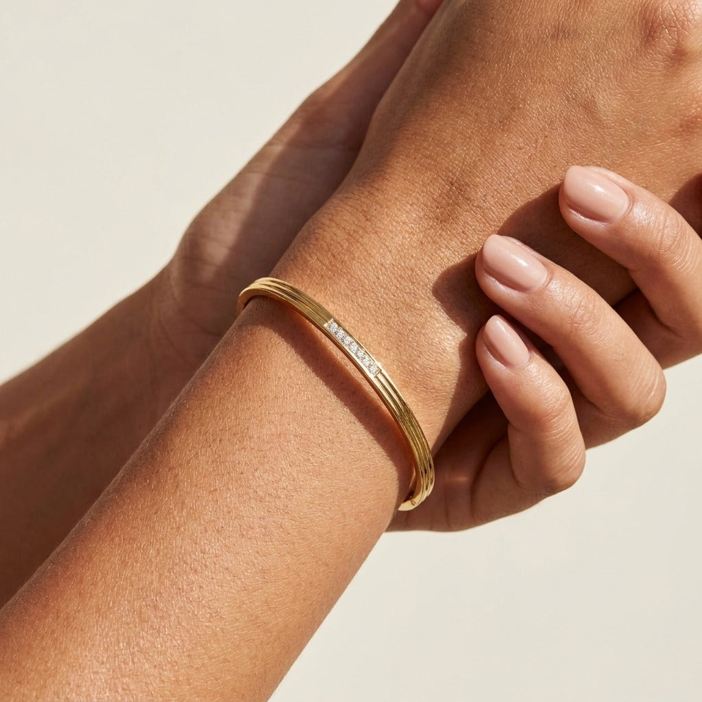 Woman wearing the Alla gold bangle with grooved lines and a row of clear crystals on the wrist