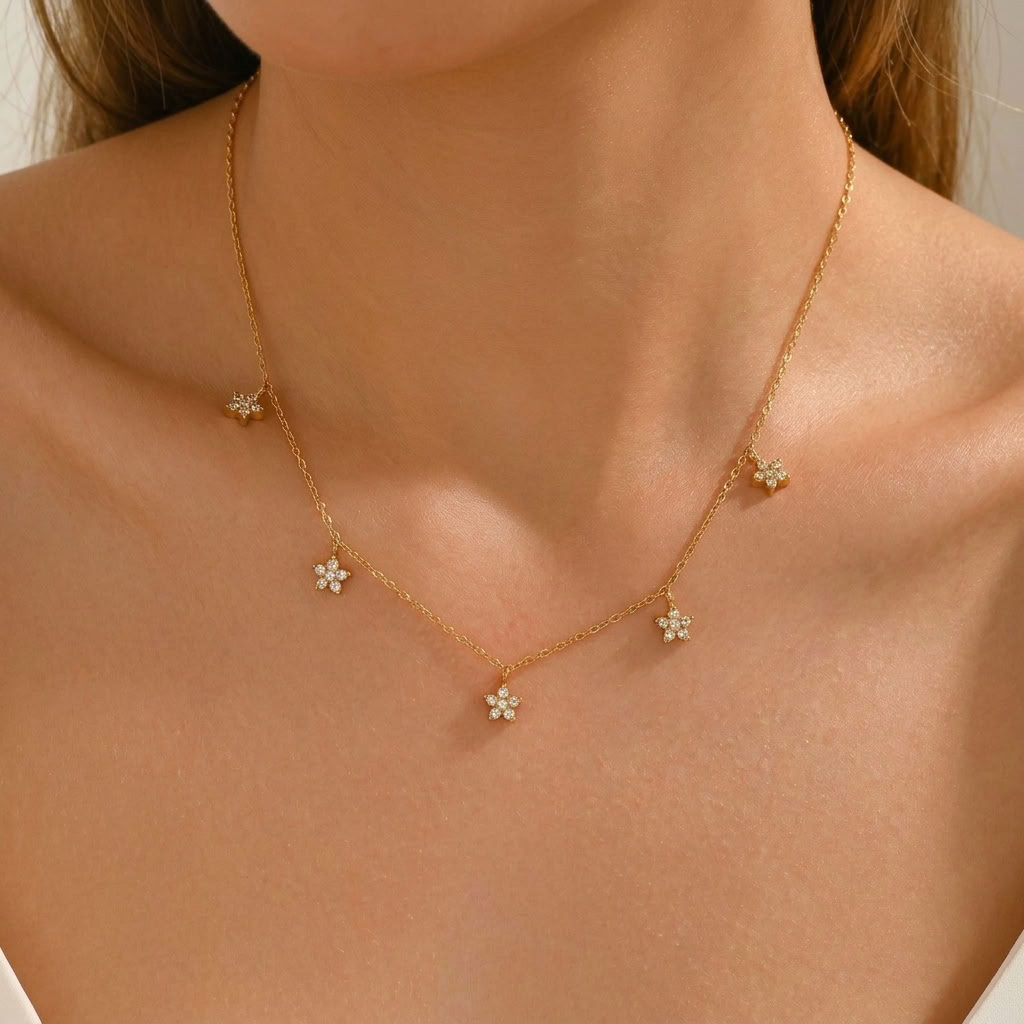 Woman wearing the Aline gold necklace with five crystal flower charms dangling at the collarbone