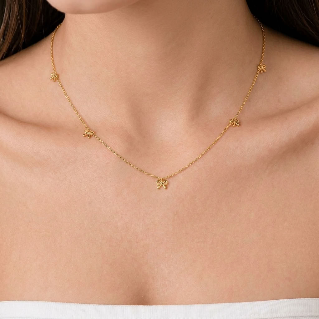 Woman wearing the Bianca gold necklace with small polished bow charms dangling along a fine chain