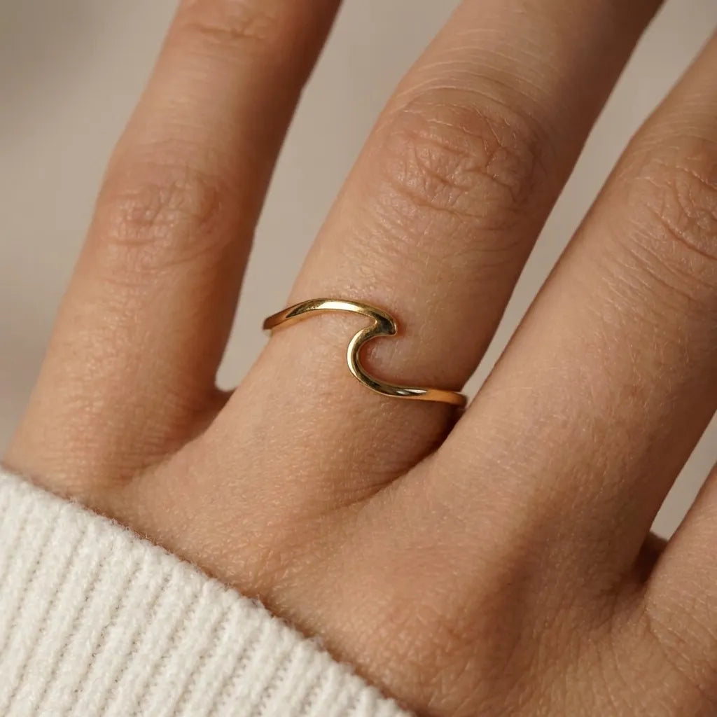 Hand wearing the slim Wave gold ring curved into a single wave, beside a cream knit sleeve