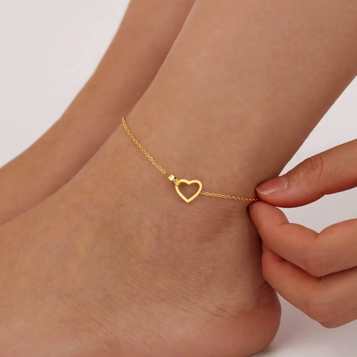 Woman holding the Élise heart link anklet in gold, an open heart set into the chain at the ankle