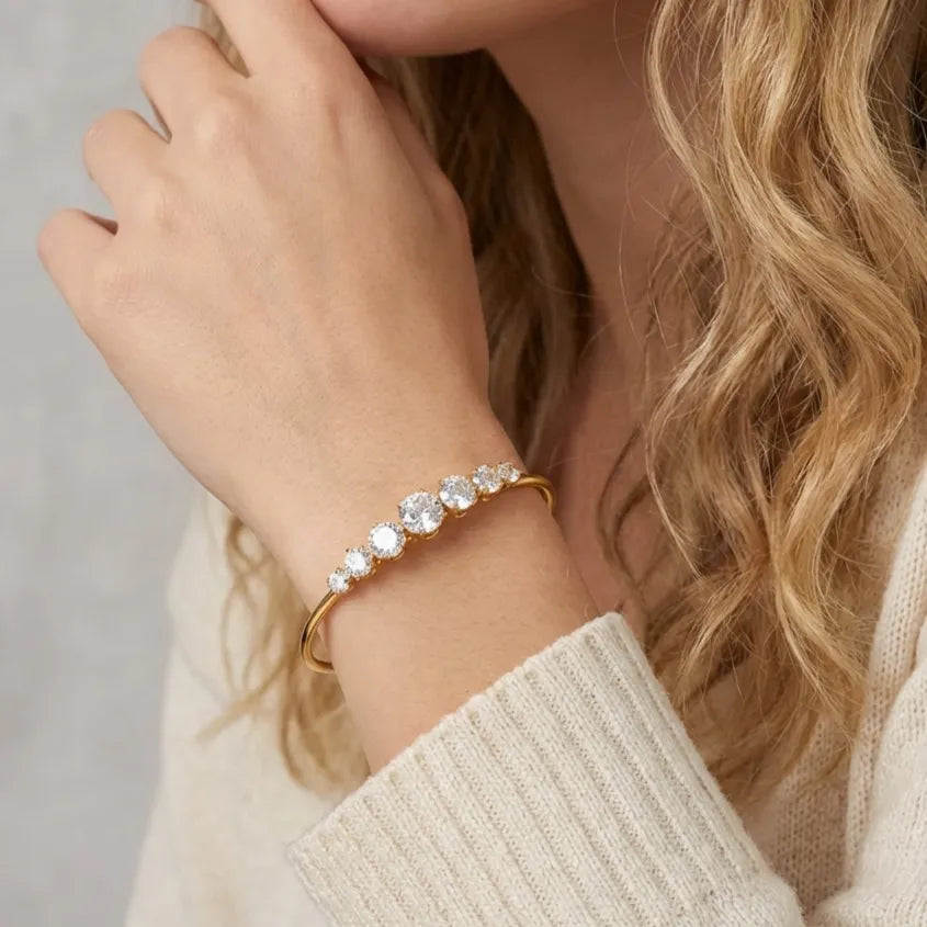 Aurélie gold bangle with a graduated row of round crystals, worn with a cream knit sweater