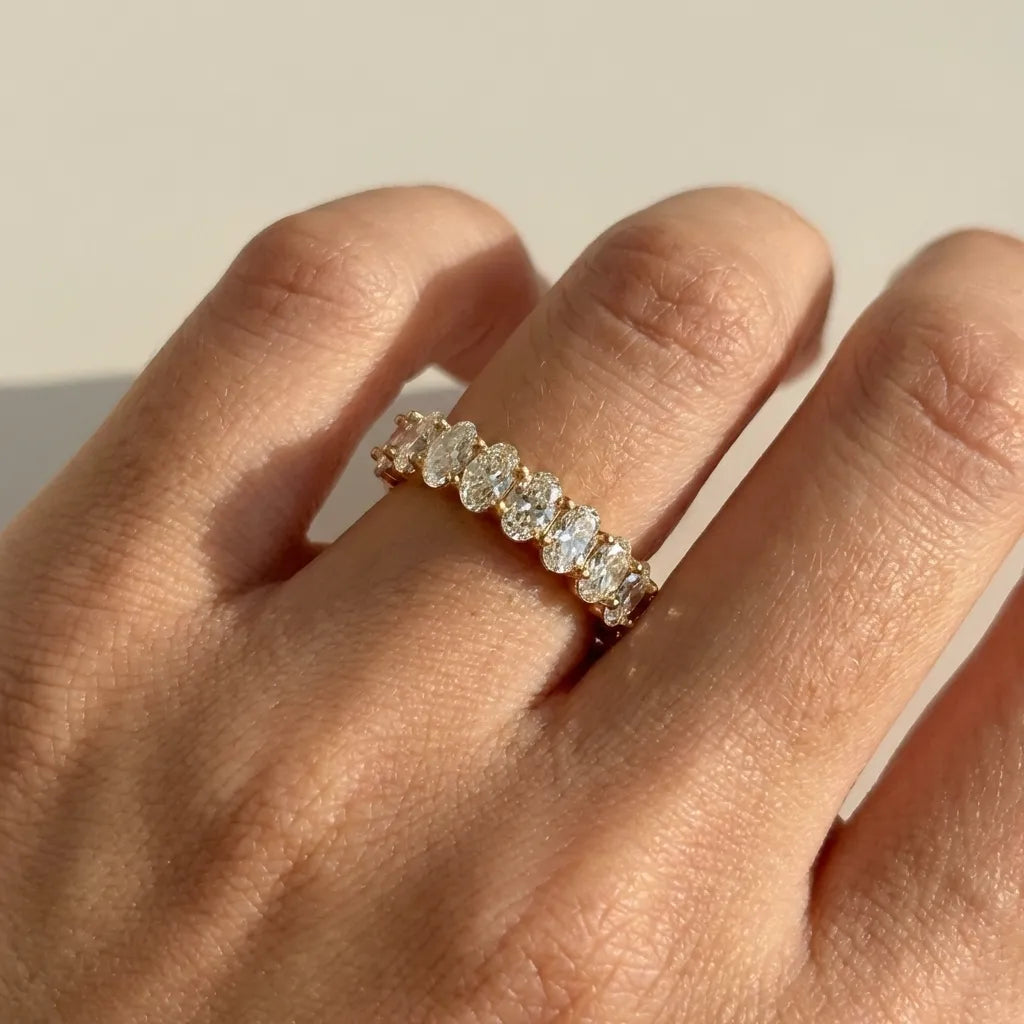 Woman wearing the Antoinette gold ring with a row of oval-cut clear crystals in sunlight