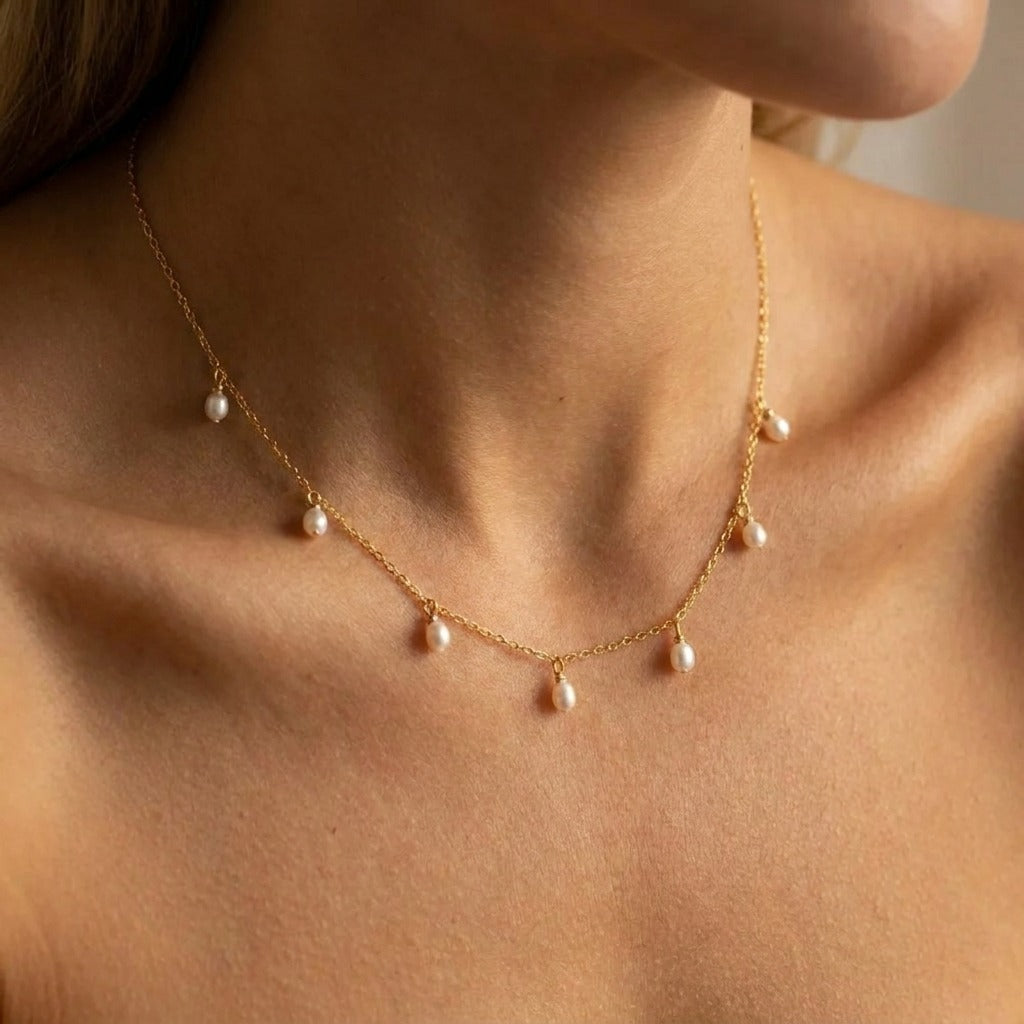 Woman wearing the Élise drop pearl necklace in gold with small oval pearls hanging from the chain