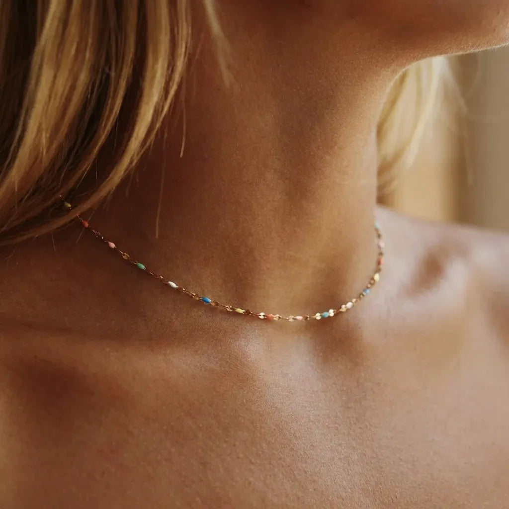 Woman wearing the Celeste gold chain choker dotted with tiny multicolored enamel beads at the throat