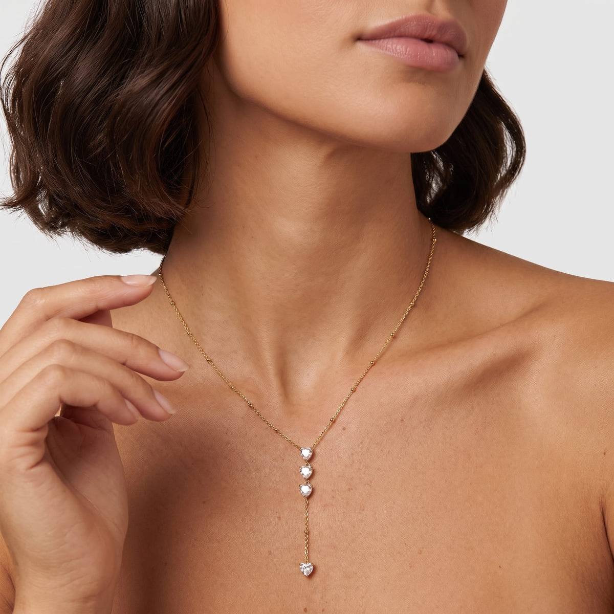 Woman wearing the Edwige stacked heart gold necklace at the collarbone while touching her hair