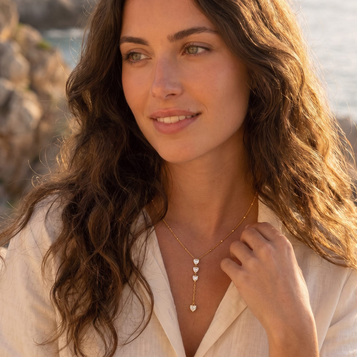 Woman wearing the Edwige stacked heart gold necklace at the collarbone in a white buttoned shirt outdoors
