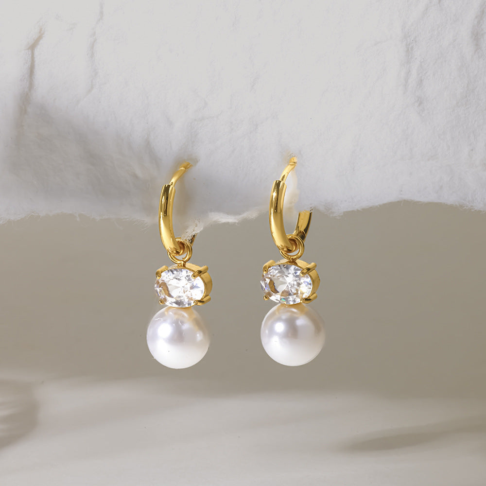 Eléonore earrings hanging from a torn paper edge, faux pearls glowing below oval crystals