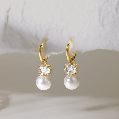 Eléonore earrings hanging from a torn paper edge, faux pearls glowing below oval crystals