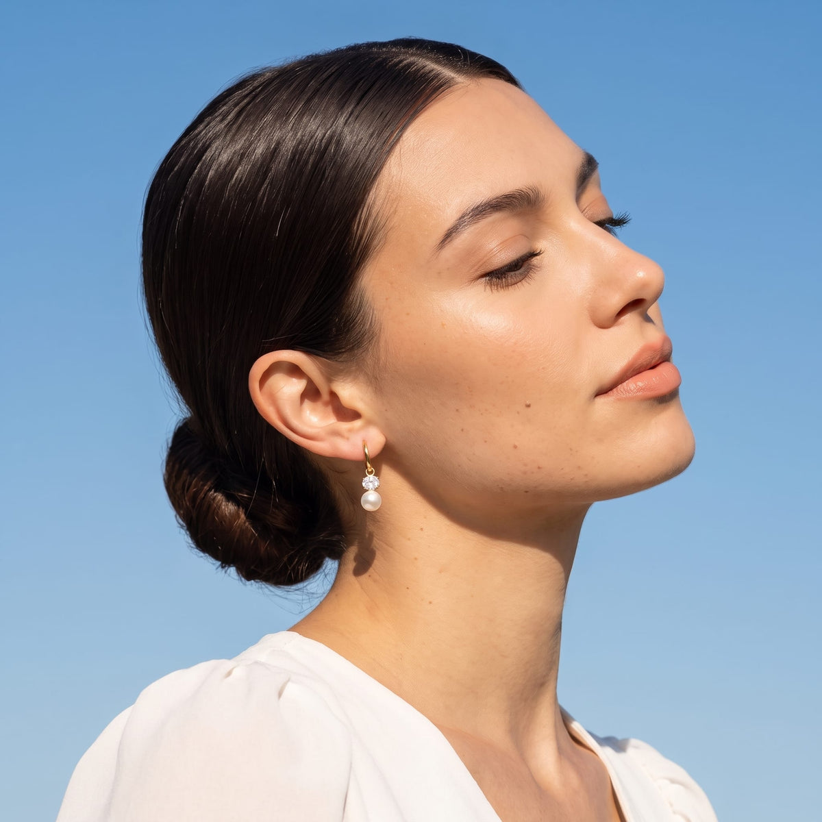 Woman wearing the Eléonore pearl drop gold earrings on the ear under blue sky