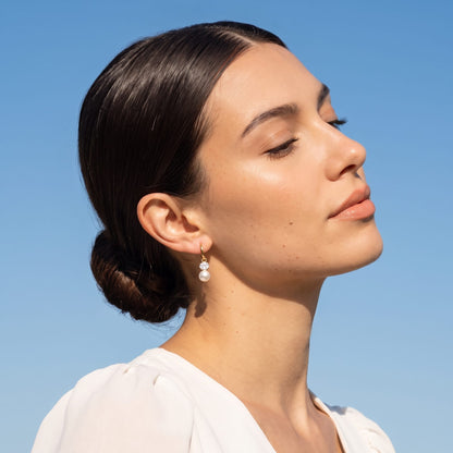 Woman wearing the Eléonore pearl drop gold earrings on the ear under blue sky