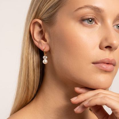 Woman wearing the Eléonore pearl drop gold earrings on the ear posing with hand